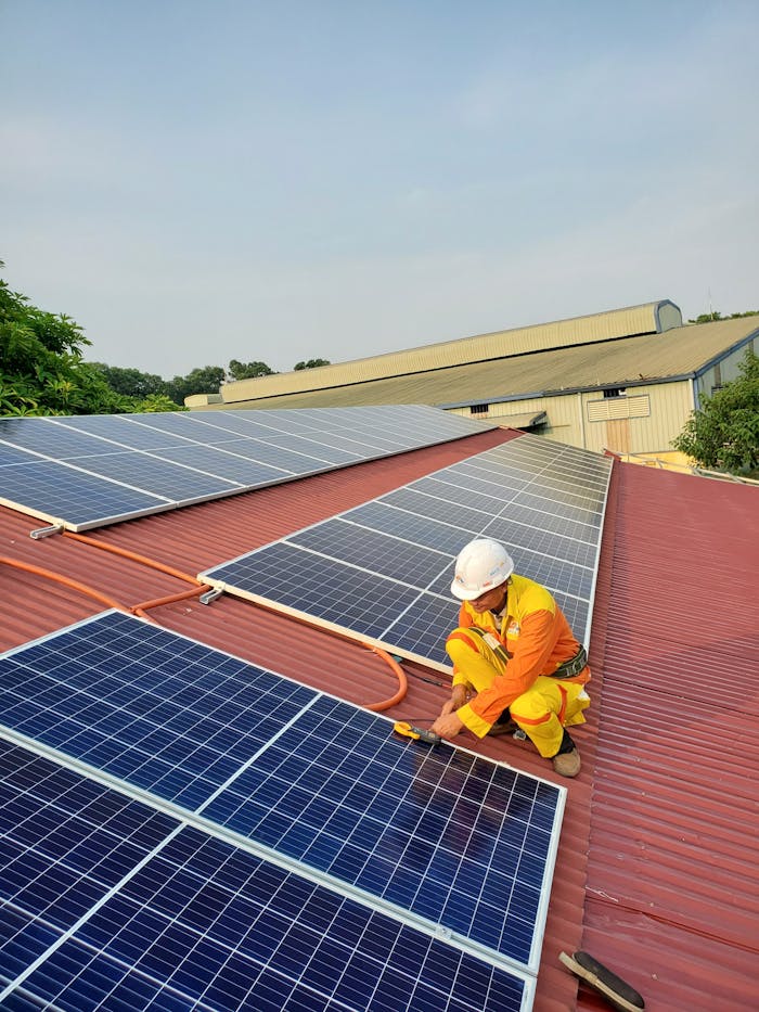 Technician working on solar panel installation on a rooftop under clear sky.